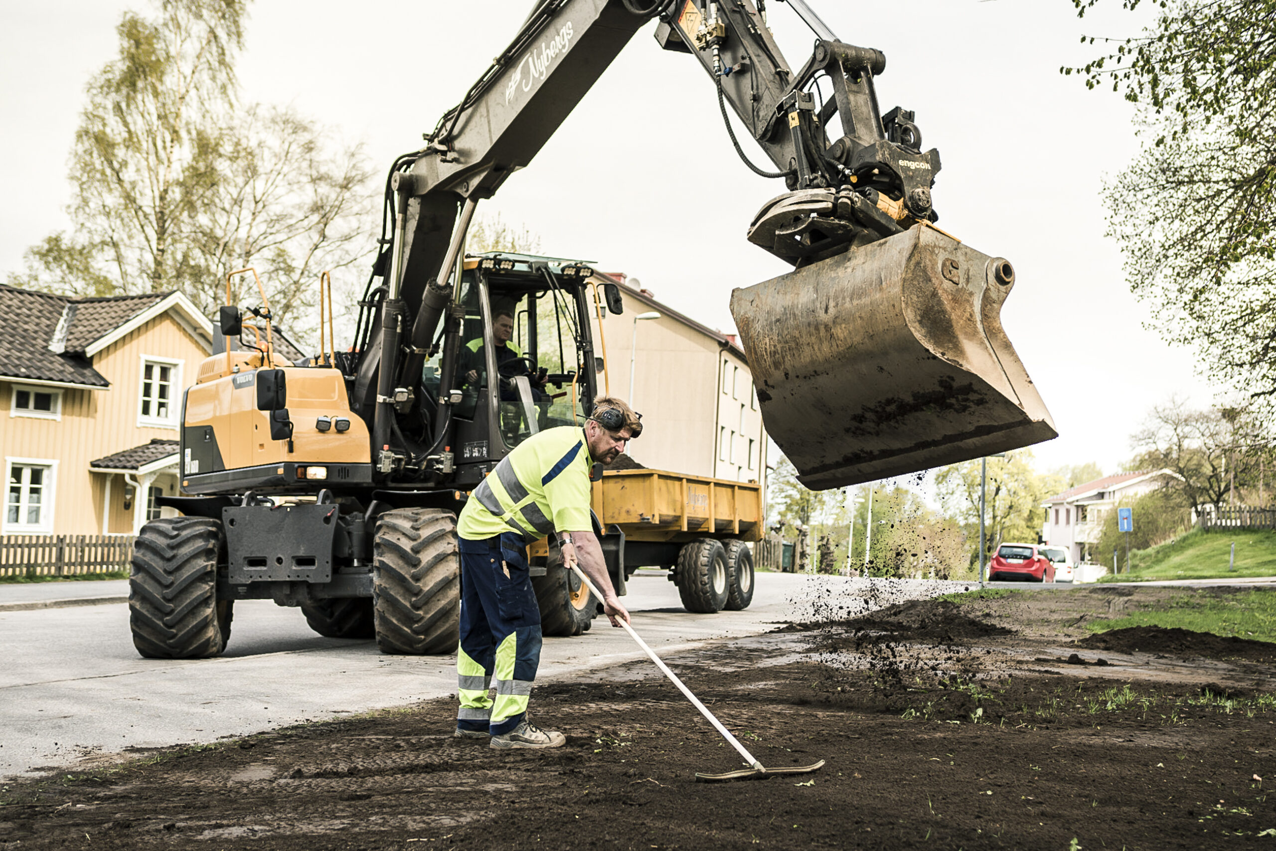 Anläggningsarbetare krattar och grävmaskin i bakgrunden